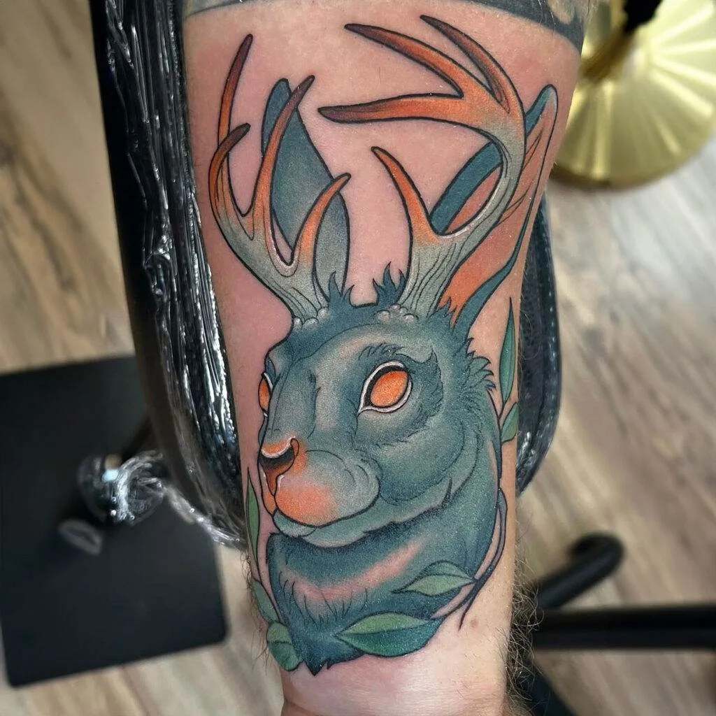 A tattoo depicting a jackalope, a mythical creature with antelope horns on a rabbit's head, featuring vivid shading and colors on a person's arm.