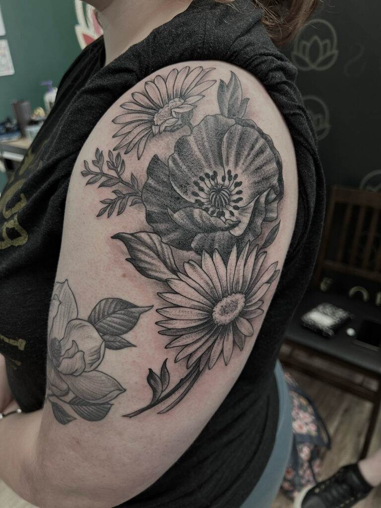 A person with a black and gray floral tattoo on their upper arm showcasing detailed flowers and leaves.