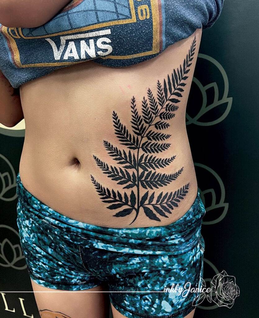 A person shows a large tattoo of a fern leaf on their side, extending from the waist to the middle of the ribcage.