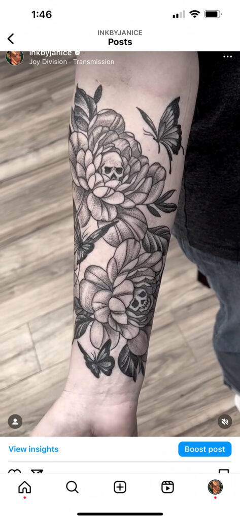 A forearm tattoo featuring detailed black and gray floral designs with skulls and butterflies.