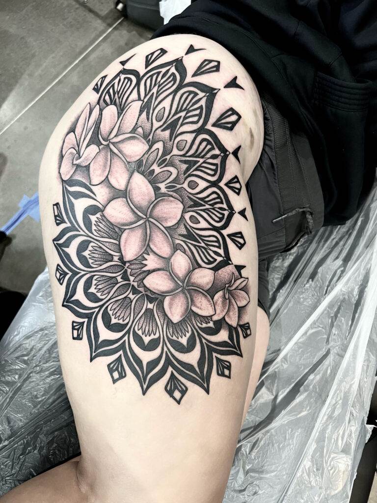 A tattoo of intricate flowers and geometric patterns on the upper thigh of an individual lying down.