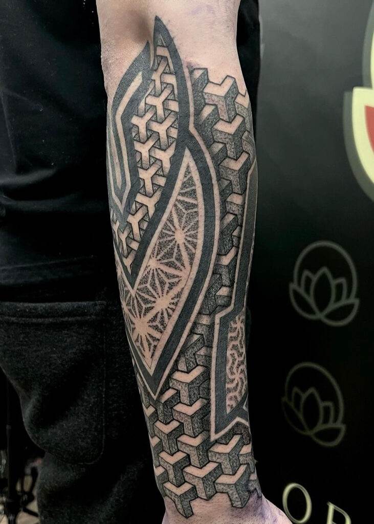 A forearm tattoo with intricate geometric patterns and interlocking shapes in black ink.