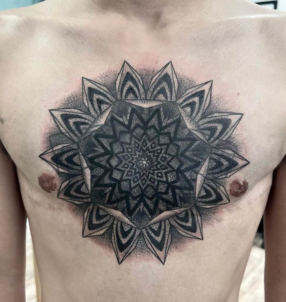 A person displaying an intricate, symmetrical mandala tattoo on their chest, positioned centrally between the nipples.