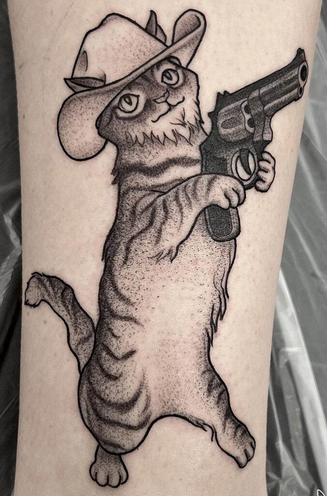 Tattoo of a standing cat wearing a cowboy hat and holding a revolver.