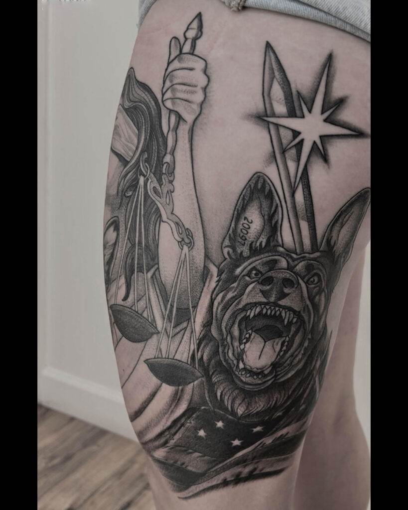 Black and white tattoo on upper thigh features a German Shepherd, Lady Justice holding scales, and a star.