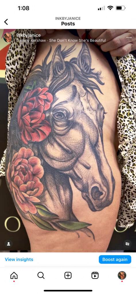 A detailed tattoo of a horse's head surrounded by red flowers, located on a person's side torso. The tattoo is black and gray with vibrant red floral elements.