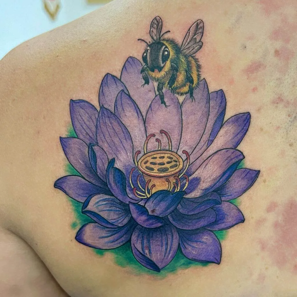 A colorful tattoo featuring a detailed bee hovering above a large, purple lotus flower on a person's skin.