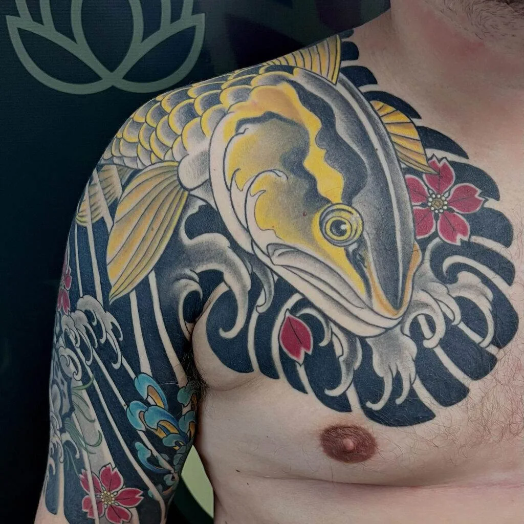 A person with a detailed shoulder and chest tattoo depicting a koi fish, floral designs, and water elements.
