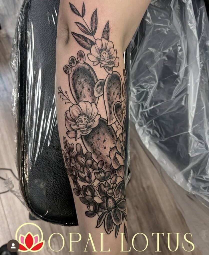 Tattoo on forearm featuring a cactus with flowers and leaves, placed on a chair.