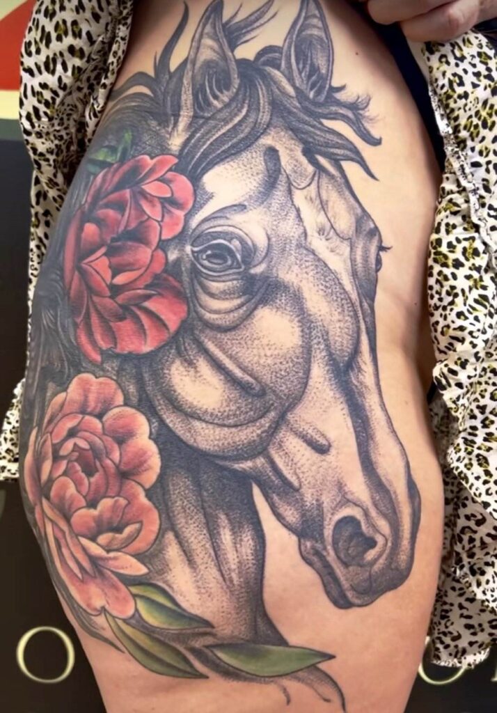 Tattoo of a horse with detailed shading and two large red flowers on a person's torso.