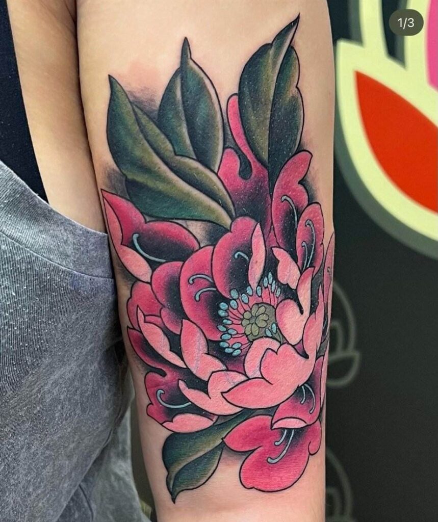 Colorful tattoo of a large pink flower with green leaves on a person's upper arm.